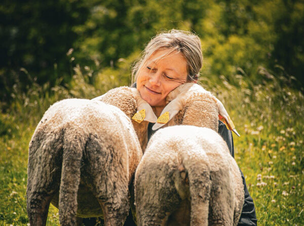 Madeleine Roediger câlinée par deux moutons dans un champ de Terre de Rêves dans l'Ain